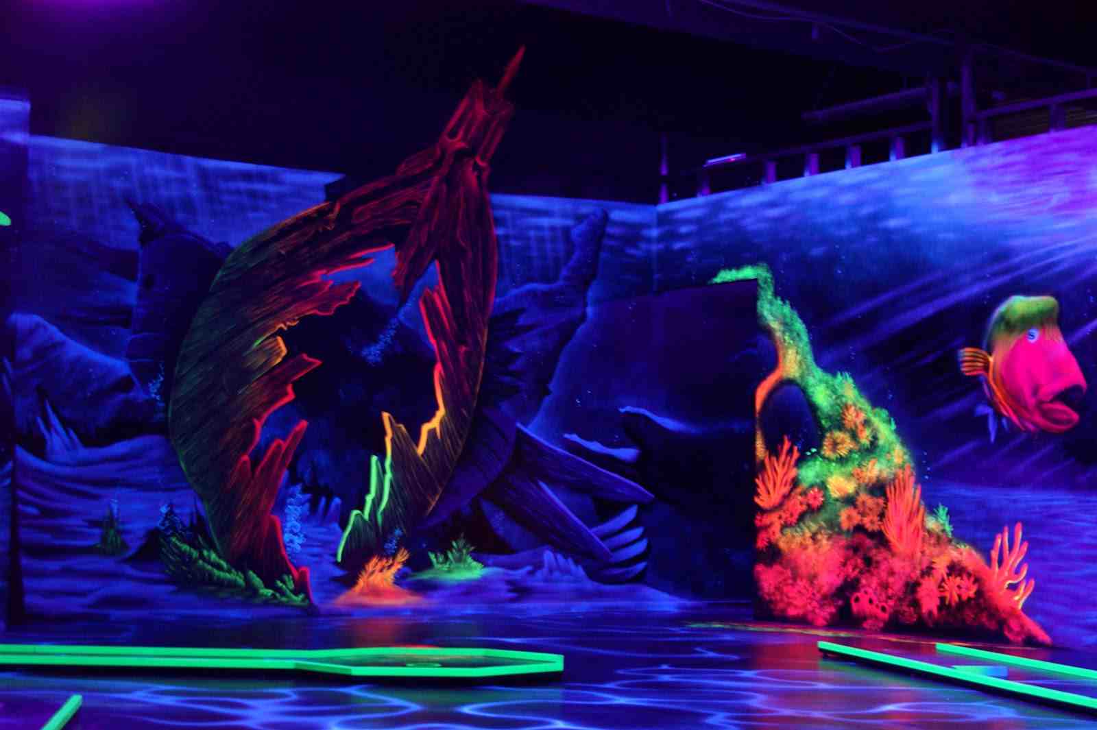 Schwarzlicht-Minigolfbahn mit leuchtendem Fisch, Korallen und gemaltem Schiffswrack in der Unterwasserwelt