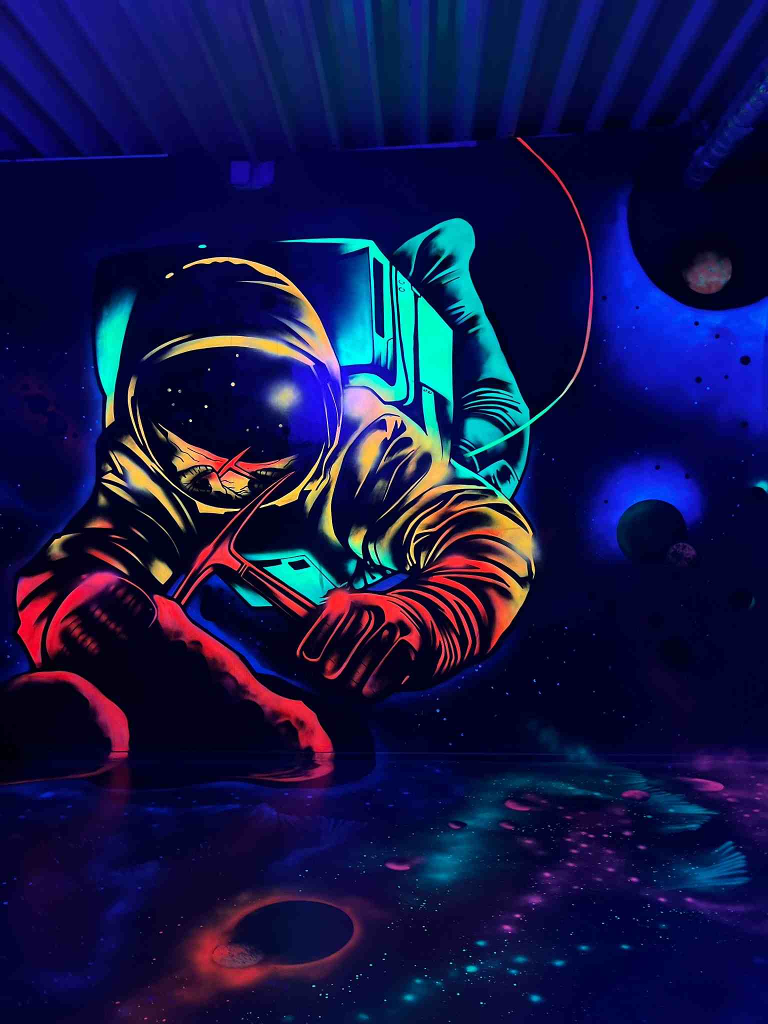 Leuchtende Schwarzlicht-Wandmalerei eines Astronauten im Weltall mit Planeten und Sternen